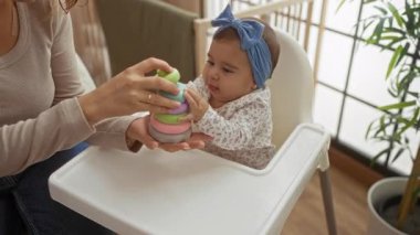Anne ve bebek rahat ev ortamında renkli oyuncaklarla oynuyor, aile sevgisi ve bebek gelişimi sergiliyor..