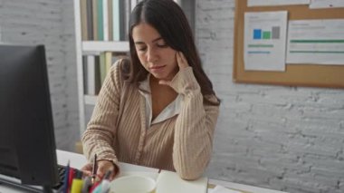 Ofisteki kadın odaklı bir defter üzerinde çalışıyor, etrafı kitaplık ve belgelerle çevrili, bir iş sırasında konsantrasyon ve içgözlem sergiliyor.