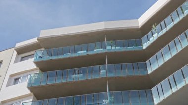 Modern cam balkonlar, açık bir ortamda çağdaş mimari ve açık hava yaşam alanlarının sergilendiği kentsel bir apartman binasında açık bir gökyüzüne karşı güneş ışığını yansıtır..