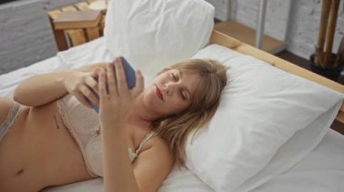 Kadın, akıllı telefon kullanırken rahat yatak odası ortamında dinleniyor, ev ortamında modern yaşam tarzını parlak ve sakin bir atmosferle tasvir ediyor..