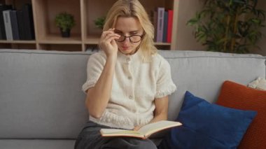 Oturma odasındaki kanepede kitap okuyan bir kadın şık dekorları ve yumuşak minderleri olan sessiz bir öğleden sonranın tadını çıkarıyor..