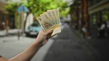 Bulanık insanlar ve binalarla dolu bir şehir caddesinde, şehir finansmanı ve açık hava para işlemlerini vurgulayan Norveçli banknotlarla el ele tutuşmak.