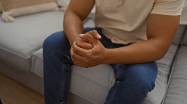 Oturma odasındaki kanepede oturan genç adam, rahat bir ev ortamında düşüncelere dalmayı ya da rahatlamayı öneriyor..