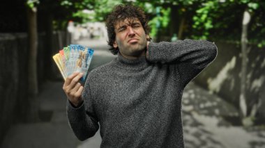 Kalabalık bir caddede İsviçre frangı banknotları tutan adam, rahatsızlığını dile getiriyor, şehir yaşamını açık havada finans temalarıyla harmanlıyor..