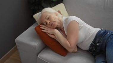 Albinizmli bir kadın, rahat bir oturma odasındaki kanepede huzurlu bir şekilde uyuyor. Kapalı bir ortamda, yumuşak doğal ışıklandırmayla rahatlık ve sükuneti vurguluyor..