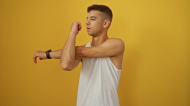 Genç İspanyol bir adam kollarını koyu sarı bir arkaplan önünde uzatıyordu beyaz bir atlet giyiyordu, modern, minimalist bir ortamda vücut bulmuş formda ve sağlıklıydı..