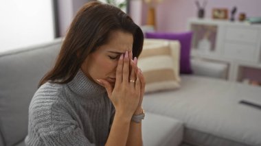 Kadın rahat bir oturma odasındaki kanepede oturup düşünceli bir İspanyol yetişkini ev ortamında sergiliyor..