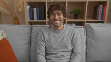 Kapalı bir kanepede rahat bir ev atmosferi sergileyen rahat bir arka planda gülümseyen genç bir adam..