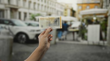 Meşgul şehir caddesinde Danimarka kronu banknotları tutan adam, arka planda bulanık arabaları ve yayaları olan açık bir şehir ortamında para gösteriyor..