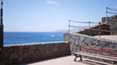 Açık hava korkuluğu ve taş duvarın bulanık görüntüsü. Lanzarote 'de okyanus kenarında çözülmüş bir bank, kanarya adaları, İspanya manzaralı bir arka plan sergiliyor.