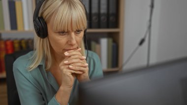 Kulaklık takan bir kadın arka planda kitap ve dosyalarla ofiste konsantre oluyor.