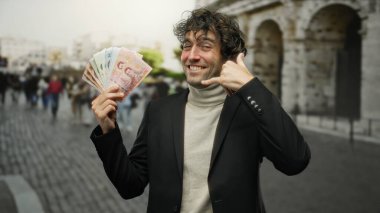 Şehirdeki bir sokakta elinde Thai banknotları tutan bir adam, bulanık bir şehir geçmişine karşı siyah bir takım elbise giymiş, parmaklarıyla mutluluk ve zenginlik sergiliyor..