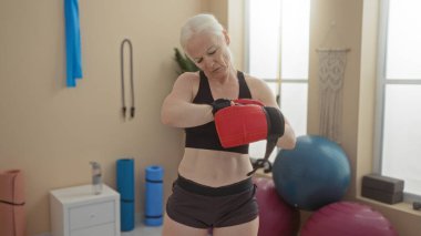 Spor salonunda boks yapmaya hazırlanan kırmızı eldivenler giyen bir kadın. Parlak ışıklı bir spor salonunda etrafı ekipmanlarla dolu bir spor salonu..