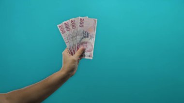 İzole edilmiş mavi arka plan duvarına karşı Türk lira banknotları tutan adamın eli, mali bağlamda para gösteriyor..