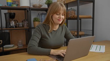 Gündüzleri rahat ve üretken bir çalışma ortamı sunan, raflar ve kahve makinesiyle çevrili, modern ofiste dizüstü bilgisayarda çalışan bir kadın..