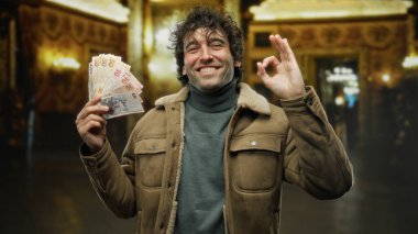 Hispanik bir adam gururla bir müzede Türk lirası sergiliyor, bir başarı jesti ile güvenle gülümsüyor, zenginliği ve başarıyı vurgulayan zarif bir dekorla çevrelenmiş..