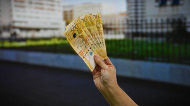 Filipin pesolarını elinde tutan adam, şehir sokakları üzerinde banknotlar tutuyor. Şehir dışındaki doğal ışık altında iş yatırımı kavramını resmediyor..