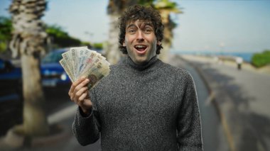 İspanyol bir adam, açık bir şehir caddesinde Czech Koruna banknotları tutuyor, arka planda palmiye ağaçları ile açık gökyüzü altında heyecan ifade ediyor, canlı bir şehir ortamı yaratıyor..