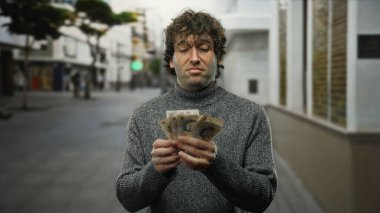 Hispanik bir adam şehrin dışında elinde İngiliz paundu tutarken düşünceli bir ifadeyle düşünceli bir finansal karar öneriyor ya da para sayıyor..