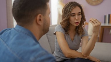 Kadın, erkekle oturma odasında konuşuyor, evde önemli konuları tartışıyor, anlamlı el hareketleri yapıyor..