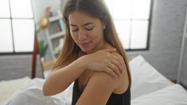 Rahat bir yatak odasında yatakta dinlenen bir kadın, nazikçe omzuna dokunan, kapalı bir ortamda sükunet ve rahatlık gösteren bir kadın..