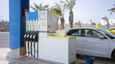 Benzin pompası çözünmüş bulanık benzin istasyonu ve açık havada park edilmiş, palmiye ağaçları ve mavi gökyüzü arka planı olan bir araba.