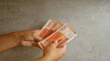 Elleri, somut bir arka plan karşısında birden fazla Norveç kronu banknotları tutan, finansal konsept ve para işleme ifadesini gösteren.
