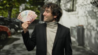 Meksika banknotlarını açık bir şehir sokağında elinde tutarak gülümseyen bir adam, günlük kıyafetlerle nakit para ve finansal başarı sergiliyor..