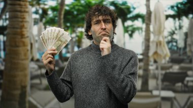 Dışarıdaki terasta, elinde Rus rublesi olan bir adam, bir kafede, sokak ortamıyla çevrili.