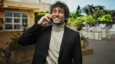 Sokakta telefon eden yakışıklı adam, açık havada gülümseyen, şık şehir modasında giyinen, çağdaş cazibesi ve gençlik enerjisiyle canlı bir şehir geçmişi öneren.