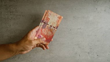 Elele tutuşan Güney Afrika rand banknotları beton arka planda renkli para ve parmakları gösteriyor