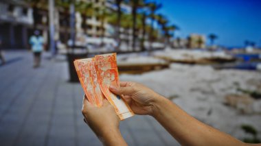 Arka planda bulanık figürler olan deniz kenarındaki sokakta Filipinli pezoları tutan eller, açık havada tatil ve finans yönetimi duygusunu yakalıyor..