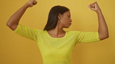Kollarını esneten genç Latin kadın parlak sarı bir arka planda poz veriyor..
