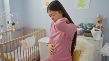 Genç Asyalı bir kadın yatakta acı içinde boynunu tutarak oturuyor. Etrafı beşikte rahat bir yatak odasıyla çevrili. Hafif ışıklandırmalı evcil ortamdaki rahatsızlığı gösteriyor.