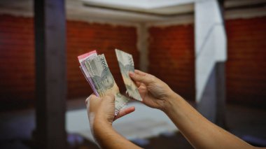 Endonezya rupiasını kapalı bir yerde tutan, şehir inşaatındaki banknotları sayan, gelişmekte olan bir ekonomideki iş faaliyetlerini yansıtan bir adam..