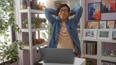 Etrafındaki raflarda çeşitli bitki ve sanat eserleri olan bir masada otururken ev dekorasyonu mağazasında rahatlayan genç bir adam.