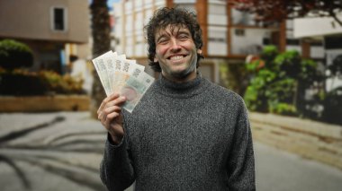 Bir şehir caddesinde elinde Czech Koruna banknotları tutarken gülümseyen İspanyol adam, şehir ortamında bir anlık neşe ve finansal başarı yakaladı..