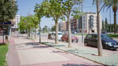 Güneşli bir banliyö bölgesinde odağını kaybetmiş arabalar, ağaçlar ve binalarla bulanık bir açık hava manzarası..