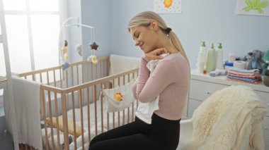 Yakınlarda bir beşiği olan rahat bir yatak odasında otururken mutlu bir şekilde gülümseyen kadın, samimi iç mekanda sıcaklığını ve sükunetini ifade ediyor..