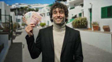 Thai banknotları tutan adam güneşli bir sokakta gülümsüyor, açık bir şehir ortamında yakalanmış, Tayland 'da canlı ve çekici bir finans teması yaratıyor..