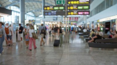 Blurred travelers walking through busy airport terminal with various signs and shops in the defocused background clipart