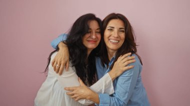 Pembe bir duvarın üzerinde kucaklaşan kadınlar, neşeli, olgun bir ortamda kardeşçe sevgi ve dostluk sergiliyorlar. Gülümseyen orta yaşlı yüzler, sıcak bir bağ ve birliktelik içinde..