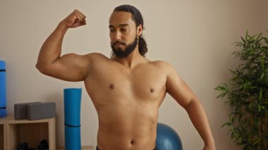 Sakallı genç adam, sağlık merkezinde kaslarını esnetiyor. Kapalı alan, spa ortamı, sakinlik, güç, zindelik, rahatlama ve sağlık odaklı.