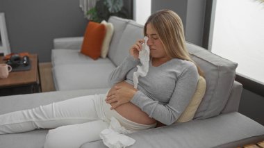 Oturma odasında oturan hamile bir kadın, kanepede dinlenirken gözyaşlarını siliyor, rahat bir ev dekoruyla çevrili, hamilelik sırasında duygularını ifade ediyor..