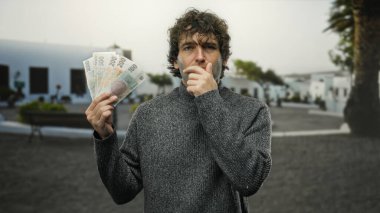 İspanyol adam, bir şehir caddesinde Czech Koruna banknotlarını incelikle tutuyor, açık şehir manzarasını ve açık hava koşullarında finansal kavramları sergiliyor..