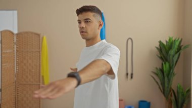 Spor salonunda egzersiz yapan genç adam esneme duruşuna ve konsantrasyonuna odaklanıyor.