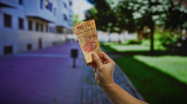 Açık şehir ortamında Meksika pezosu tutan bir adamın eli hareketli bir şehir ortamında yatırım ve iş fırsatları öneriyor..