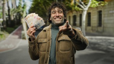 İspanyol adam canlı bir şehir caddesinde Türk lirasını coşkuyla tutuyor, neşeli bir ifadeyle para gösteriyor..