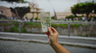 Bir şehir caddesinde tek kişilik banknotlarla el ele tutuşmak, çeşitli mimari ve bulanık arkaplanı olan bir şehir ortamındaki finansal temaları vurgulamak.