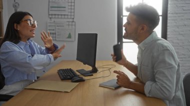 Ofisteki adamla konuşan bir kadın, masada bilgisayarla, belgelerle ve akıllı telefonla iş görüşmeleri yapıyor.